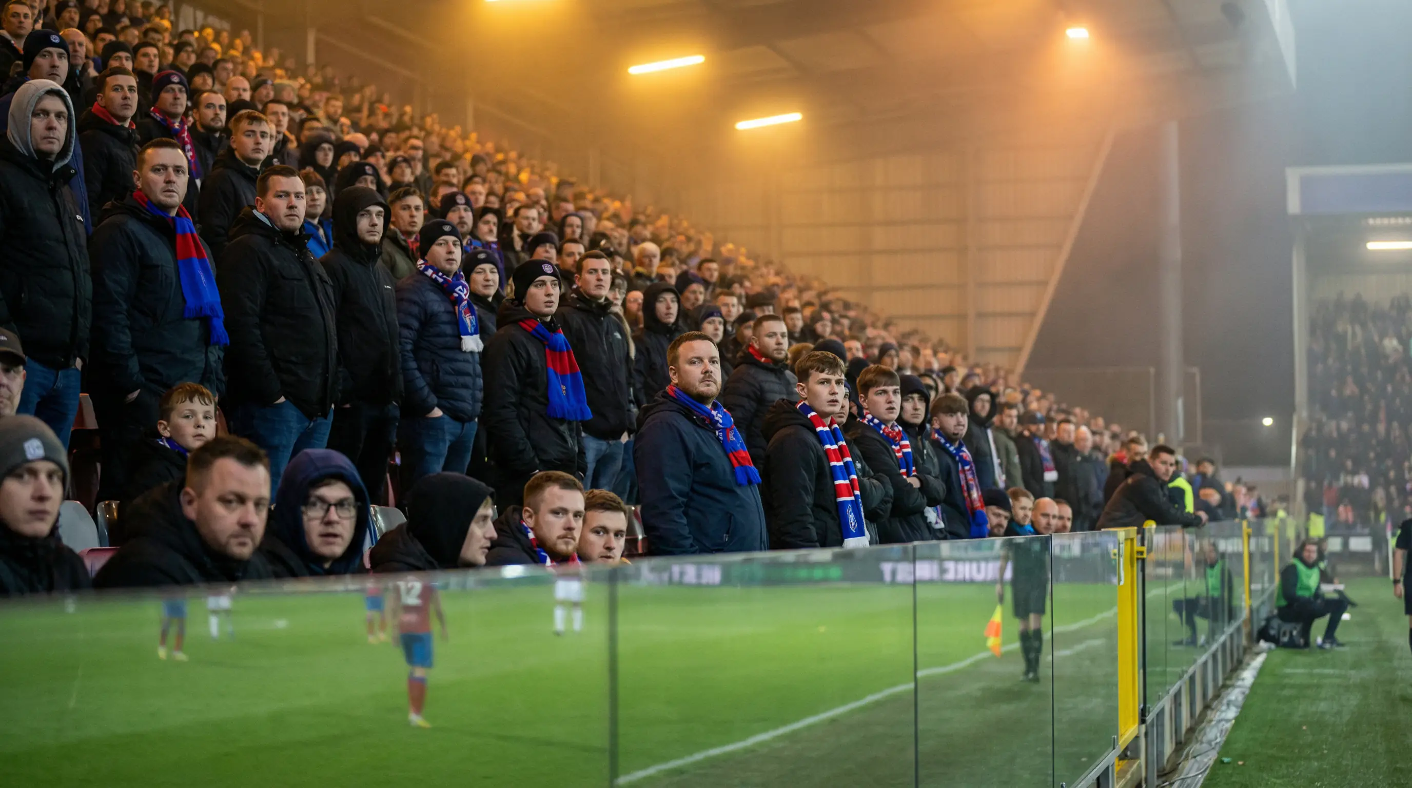 Futbola līdzjutēji skatās spēli no stadiona tribīnēm vakarā
